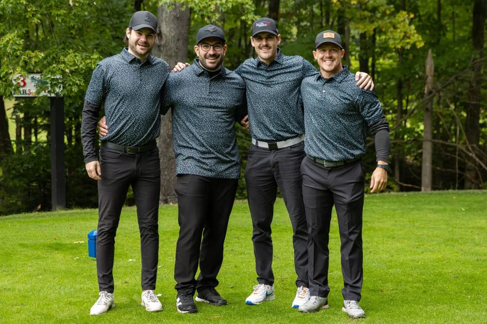Quatre golfeurs en polos assortis et casquettes foncées, alignés au départ