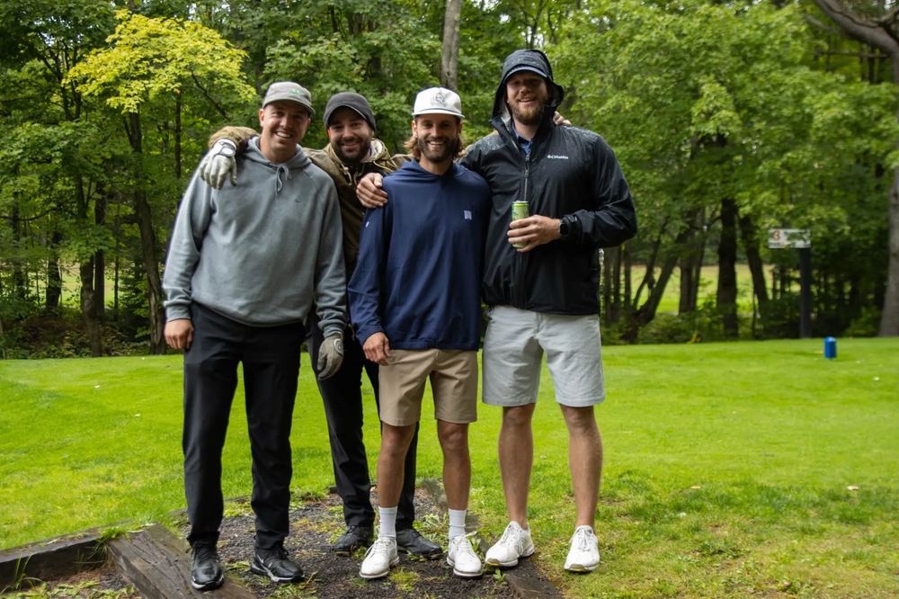 Quatre golfeurs au départ, l'un d'eux en imperméable à capuchon sous la pluie